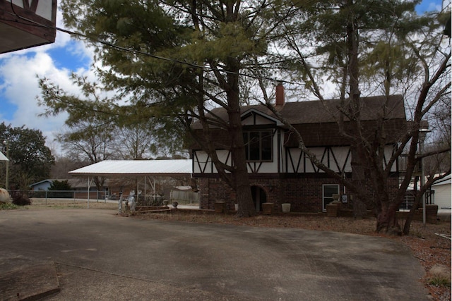 exterior space with brick siding, a chimney, fence, a carport, and driveway