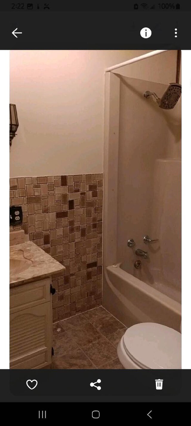 full bath with wainscoting, toilet, bathing tub / shower combination, tile patterned floors, and tile walls