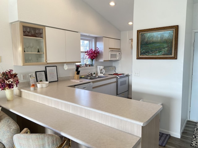 kitchen featuring white appliances, lofted ceiling, sink, a kitchen bar, and kitchen peninsula