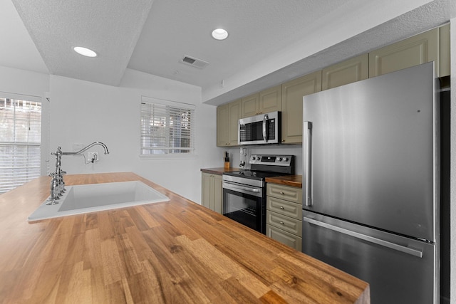 kitchen with sink, green cabinets, stainless steel appliances, and butcher block counters