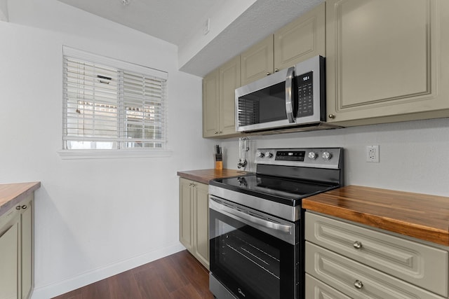 kitchen featuring butcher block countertops, stainless steel appliances, cream cabinetry, and dark wood-type flooring