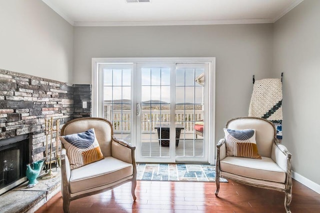 sitting room with ornamental molding, a stone fireplace, and wood finished floors