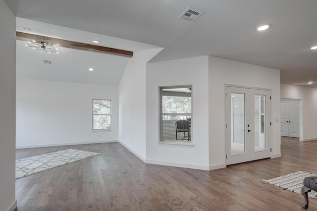 empty room featuring lofted ceiling with beams, a chandelier, french doors, and hardwood / wood-style floors