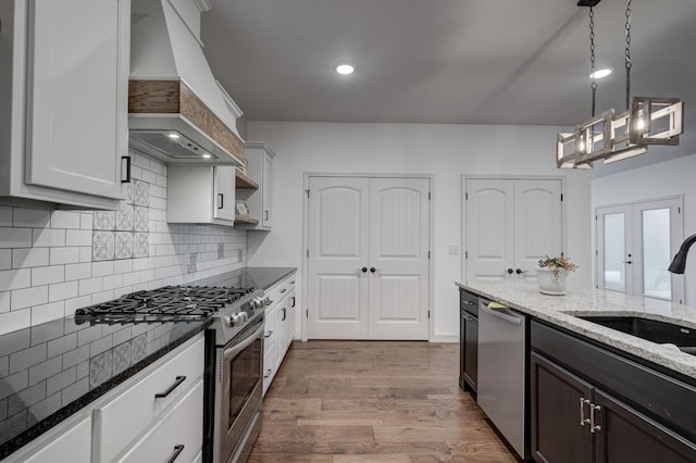 kitchen with custom exhaust hood, white cabinets, appliances with stainless steel finishes, and pendant lighting