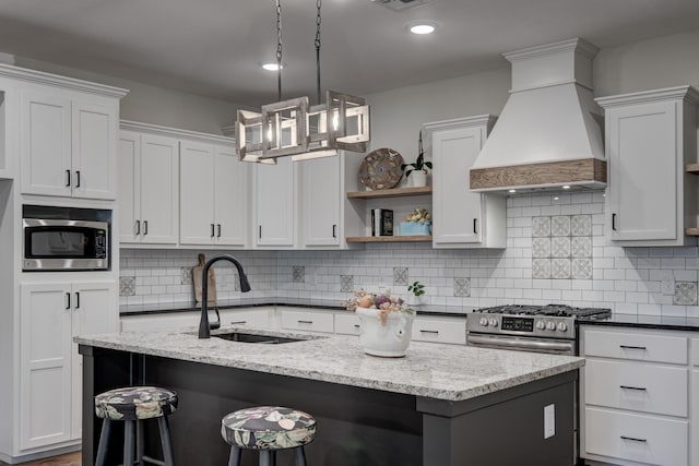 kitchen with appliances with stainless steel finishes, premium range hood, dark stone counters, pendant lighting, and sink