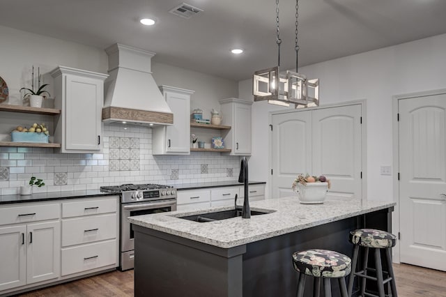 kitchen featuring custom range hood, stainless steel gas stove, sink, white cabinetry, and dark stone countertops