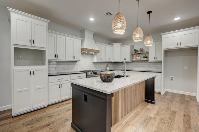 kitchen with a center island with sink, decorative light fixtures, light stone countertops, custom range hood, and white cabinets