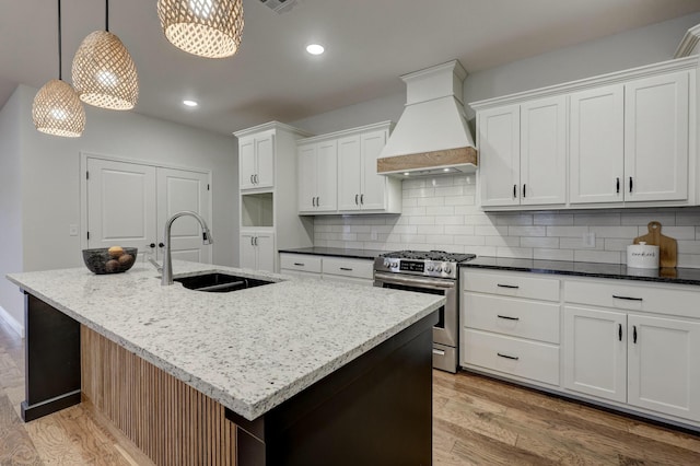 kitchen featuring gas range, an island with sink, and premium range hood