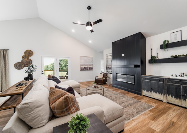 living room featuring high vaulted ceiling, light hardwood / wood-style flooring, ceiling fan, and a fireplace