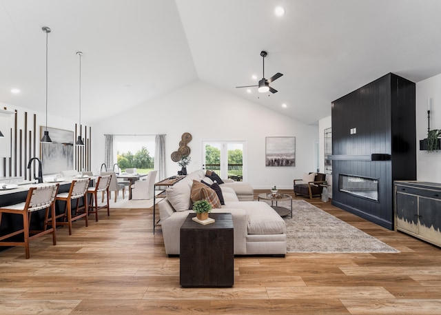 living room with light hardwood / wood-style floors, high vaulted ceiling, ceiling fan, and a large fireplace