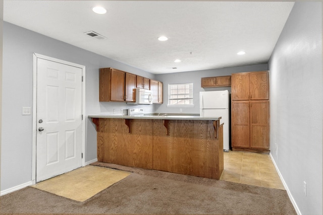 kitchen featuring white appliances, light carpet, a breakfast bar, and kitchen peninsula