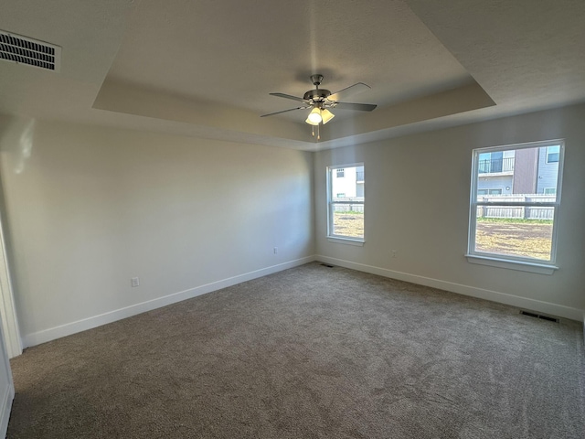 empty room with carpet, ceiling fan, and a raised ceiling