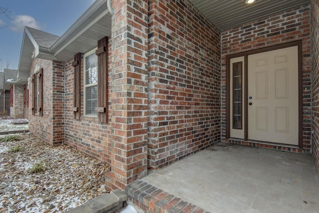 entrance to property featuring roof with shingles, a chimney, and brick siding