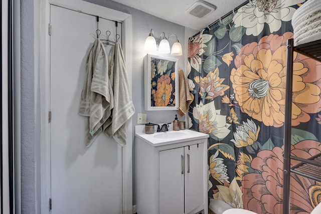 full bath featuring visible vents, a textured wall, and vanity