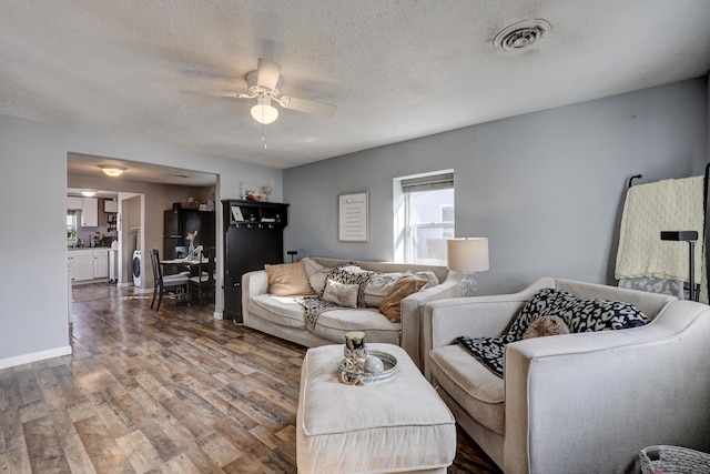 living room with baseboards, visible vents, a ceiling fan, wood finished floors, and a textured ceiling