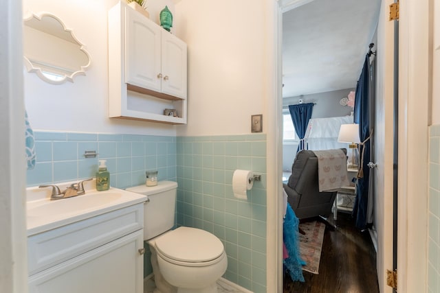 bathroom with a wainscoted wall, tile walls, toilet, vanity, and wood finished floors