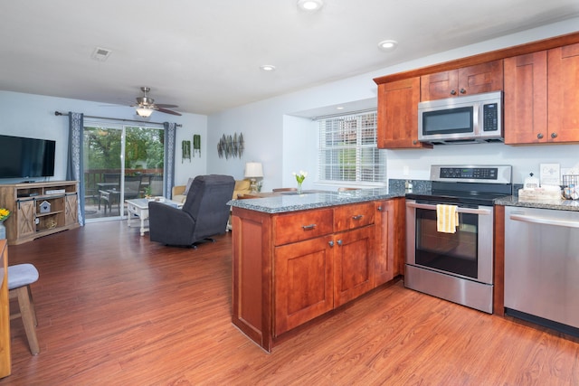 kitchen with appliances with stainless steel finishes, dark stone counters, open floor plan, and light wood-style flooring