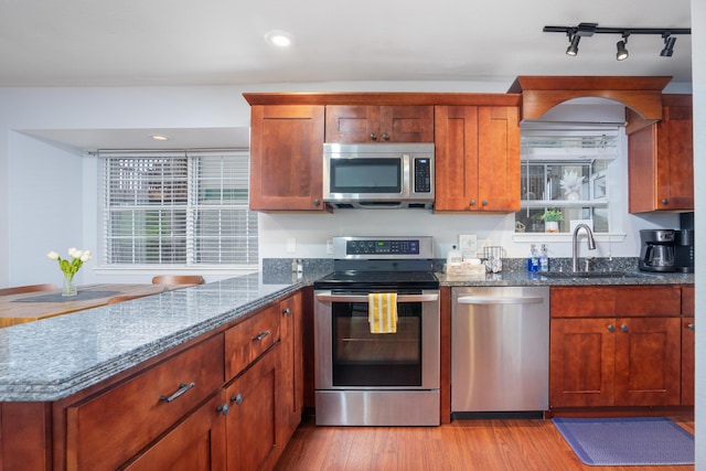 kitchen with appliances with stainless steel finishes, light wood-style floors, a sink, and dark stone countertops