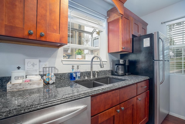 kitchen with stainless steel appliances, baseboards, a sink, and dark stone countertops