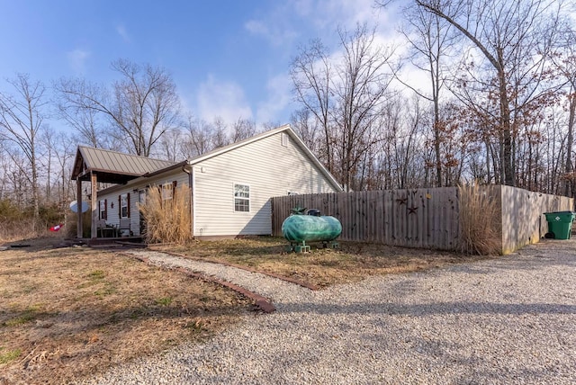 view of side of home with metal roof, heating fuel, and fence