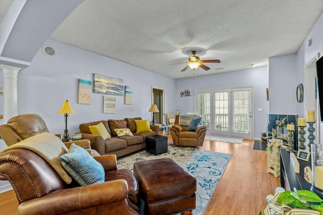 living area with ornate columns, light wood-style flooring, a textured ceiling, and a ceiling fan