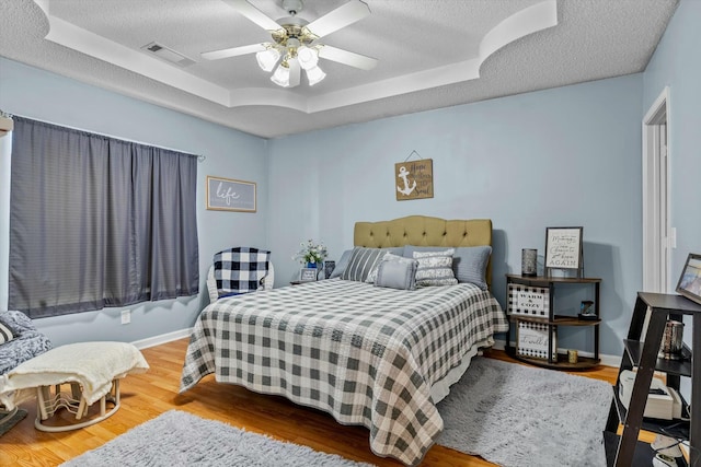 bedroom featuring a raised ceiling, visible vents, a textured ceiling, wood finished floors, and baseboards