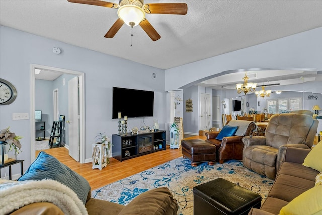 living area featuring arched walkways, a textured ceiling, wood finished floors, baseboards, and ceiling fan with notable chandelier