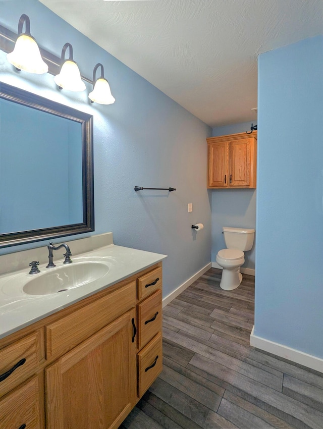 bathroom with baseboards, toilet, wood finished floors, a textured ceiling, and vanity