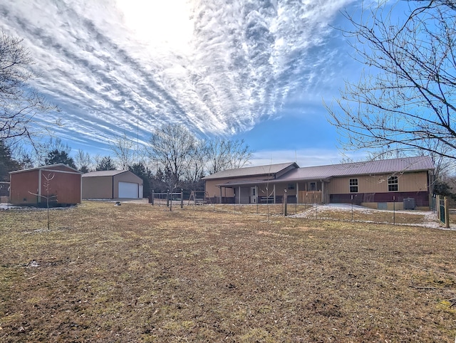 view of front of property featuring an outbuilding, metal roof, a detached garage, fence, and a front lawn