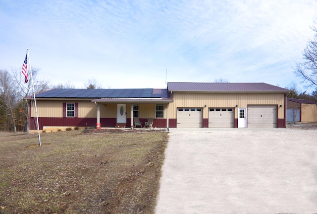 view of front of house with metal roof, covered porch, a garage, driveway, and roof mounted solar panels