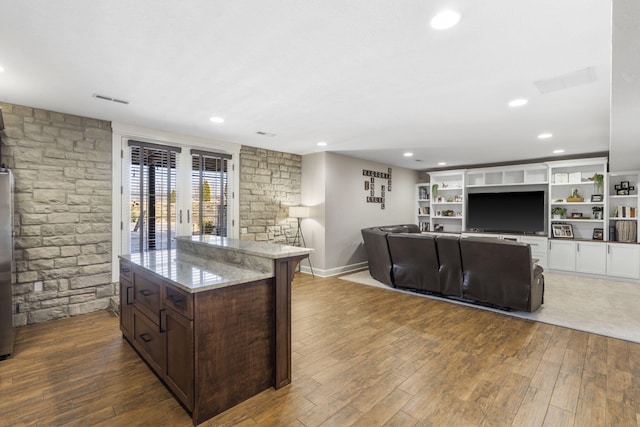 kitchen with light stone counters, open floor plan, dark brown cabinetry, and wood finished floors