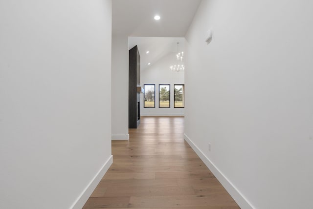 hall with baseboards, light wood-type flooring, high vaulted ceiling, a notable chandelier, and recessed lighting