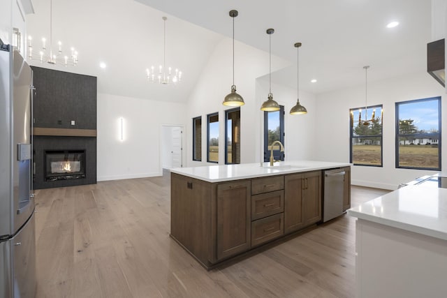 kitchen with a center island with sink, stainless steel appliances, light countertops, a chandelier, and pendant lighting