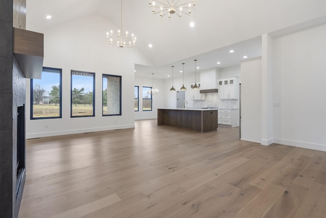 unfurnished living room featuring high vaulted ceiling, a notable chandelier, a sink, baseboards, and light wood finished floors