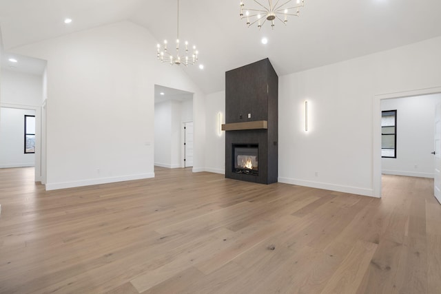 unfurnished living room with a large fireplace, light wood finished floors, baseboards, a chandelier, and high vaulted ceiling