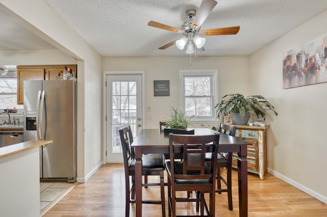 dining area with light wood-style flooring, baseboards, ceiling fan, and a textured ceiling