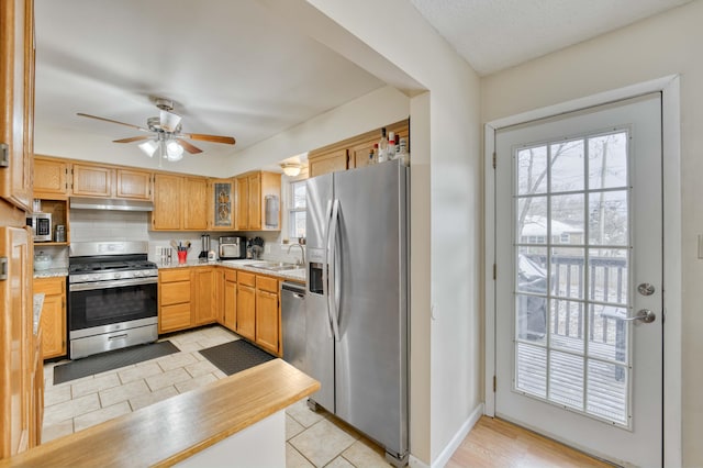 kitchen featuring stainless steel appliances, light countertops, under cabinet range hood, and a ceiling fan