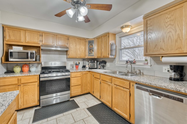 kitchen with stainless steel appliances, backsplash, a sink, light stone countertops, and under cabinet range hood