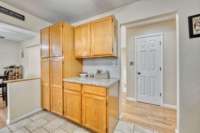 kitchen featuring light tile patterned floors, baseboards, decorative backsplash, light stone counters, and light brown cabinets