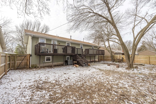 snow covered house with a fenced backyard, stairway, a wooden deck, and central AC unit