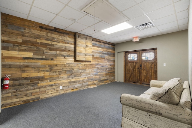 interior space featuring carpet floors, wood walls, a drop ceiling, and visible vents