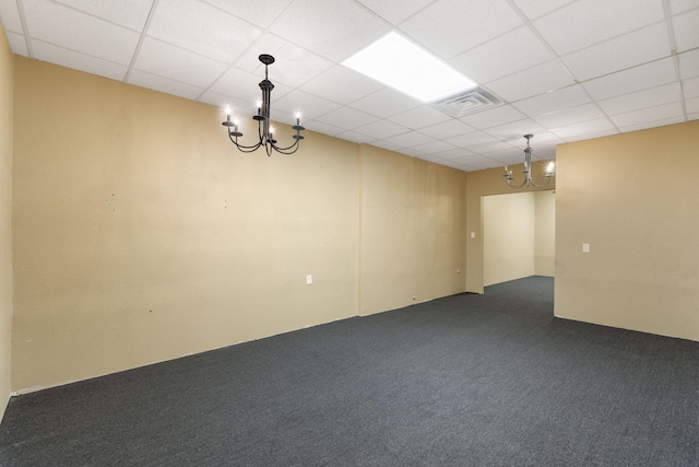 spare room featuring dark colored carpet, visible vents, a notable chandelier, and a drop ceiling