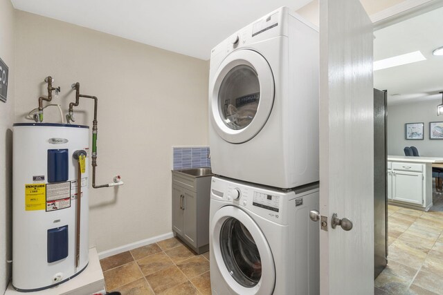 laundry room featuring cabinet space, baseboards, stacked washer and clothes dryer, and electric water heater