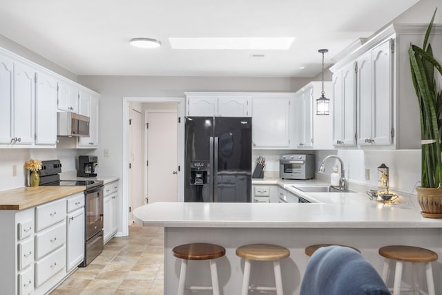 kitchen with a peninsula, a kitchen breakfast bar, light countertops, black appliances, and decorative light fixtures