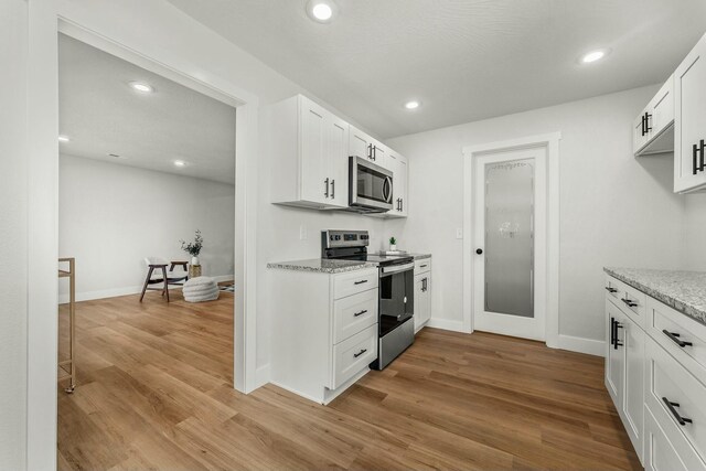 kitchen featuring appliances with stainless steel finishes, light wood-type flooring, light stone countertops, and white cabinets