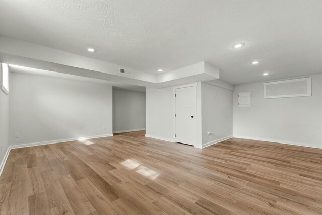 finished below grade area with light wood-style floors, baseboards, visible vents, and recessed lighting