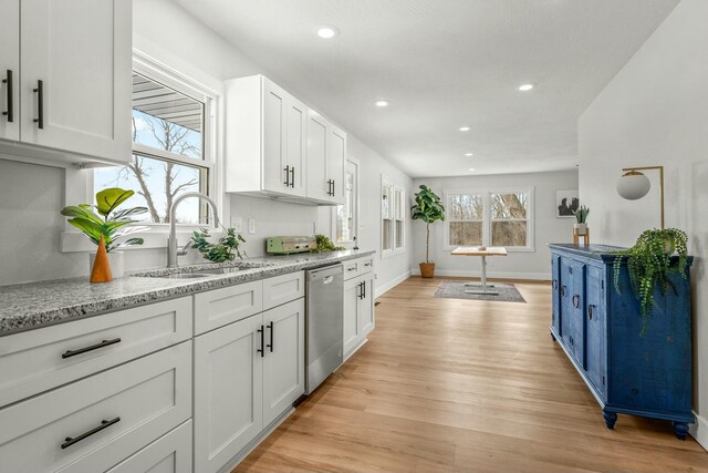 kitchen featuring light wood finished floors, white cabinets, light stone countertops, stainless steel dishwasher, and a sink