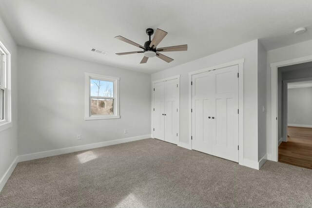 unfurnished bedroom featuring carpet floors, a ceiling fan, baseboards, visible vents, and multiple closets