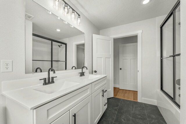 bathroom with double vanity, baseboards, bath / shower combo with glass door, and a sink