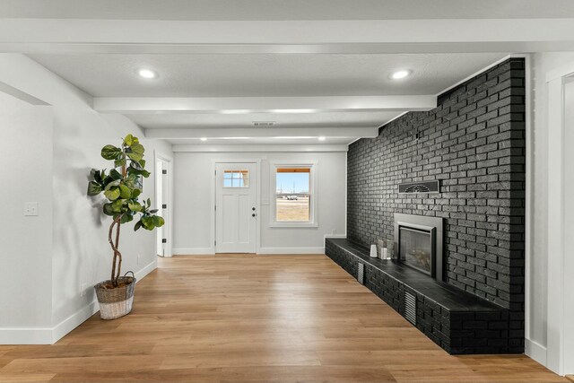 foyer entrance featuring a brick fireplace, baseboards, and light wood finished floors